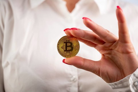 Virtual cryptocurrency money Bitcoin golden coin in the left hand of a woman with red nail polish.