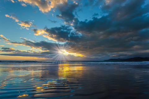 Sunrise over the ocean. Gentle cloud colors are reflected in the ocean water. Light wind causes