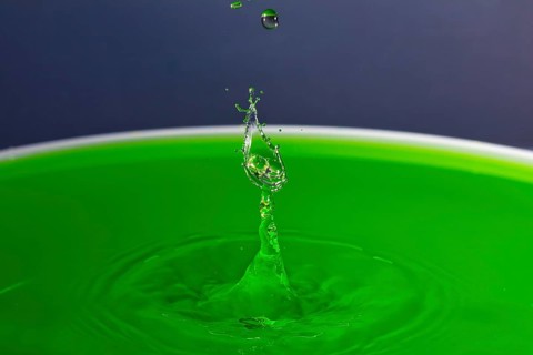 A drop of water forms a splashing sculpture on green liquid, water droplets, collision, high-speed