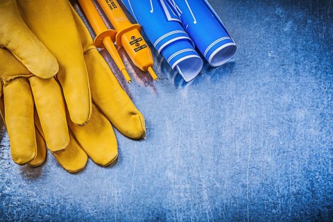 Yellow electrical tester safety gloves blue construction drawings on metallic background
