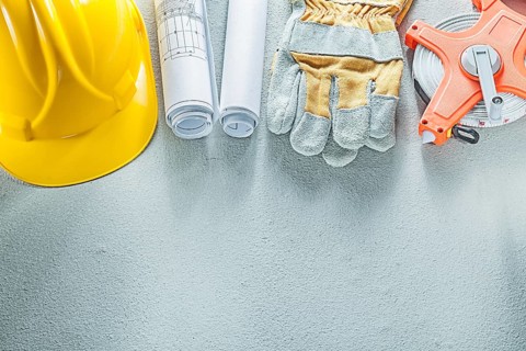 Safety gloves hard hats blueprints measuring tape on concrete background