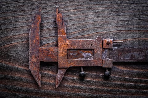 Rusted old-fashioned measuring slide caliper on vintage wooden board construction concept