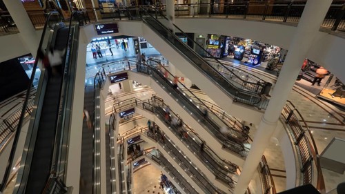 Customers in trade centre riding escalators. View from upper to lower floor. Shopping mall of