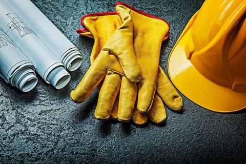 Working gloves with yellow helmet and rolled blueprints