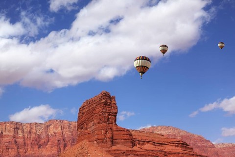Huge balloons with the passenger basket flying over the picturesque cliffs of red sandstone