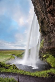 Sunny day in Iceland. Seljalandsfoss waterfall in July. Large rainbow decorates a drop of water.