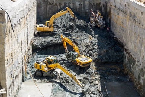 Excavators dig at a construction site of a street and a subway. Baggers transport dirt to a higher