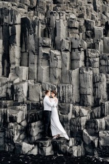 A wedding couple stands on a wall of stone pillars. The bride and groom are hugging on basalt