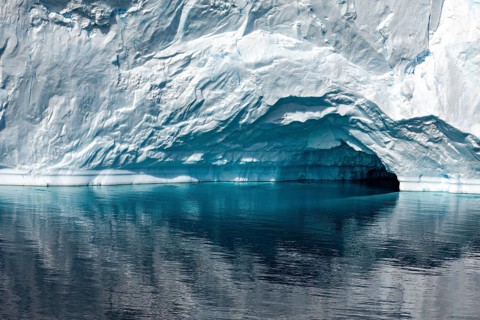 A large iceberg with a small cave is reflected in the calm, reflective water, icebergs in the