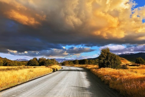 The huge cloud lit yellow-orange rays of sunset. Gravel road through the Patagonian steppe