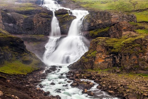 Powerful streams of cascade falls with a roar break against cold rocks. Cold and rainy July in