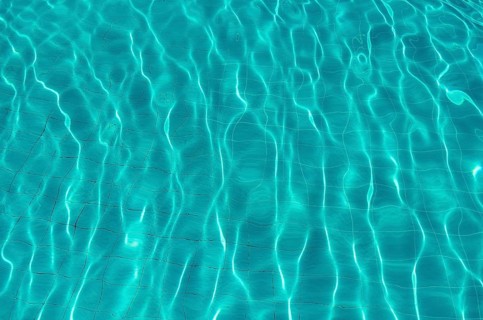 Waves on the light of the pool water. Swimming pool with blue water. Water surface texture. View
