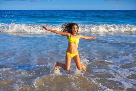 Bikini teen girl jumping happyt in Caribbean sunset beach splashing shore