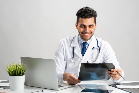 Handsome doctor looking at x-ray scan. Happy physician in white coat with stethoscope sitting at