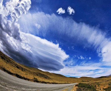 Gray dirt road in the Chilean national park to Torres del Paine. Improbable form the clouds created