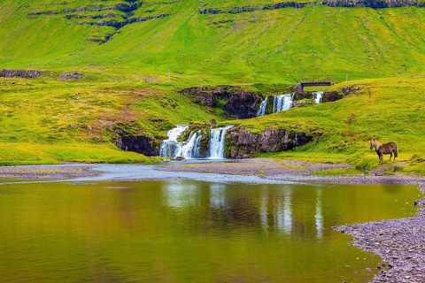 Mountains and waterfalls. Cloudy day in Iceland. Cascade Falls on the green grassy hill