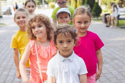 Portrait of happy preschool kids posing closely together outdoors, looking at camera. Lovely boy