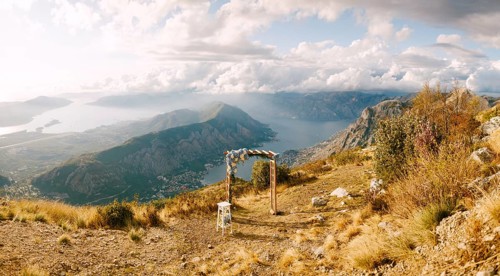 Simple wooden arch decorated with flowers stands on top of a mountain overlooking the valley.