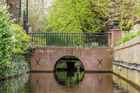 Small canal with a brick arch bridge and lush vegetation along the banks, den haag, the netherlands