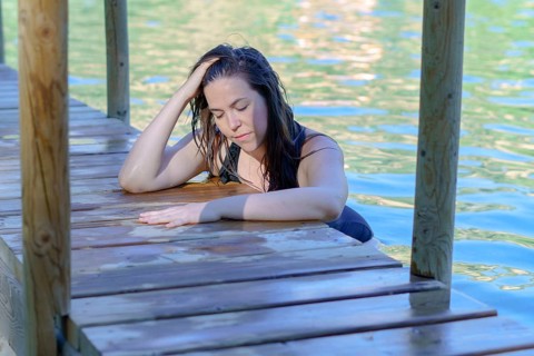 Beautiful woman bathing in a lake with her hands folded on a wooden pier looking at the sun