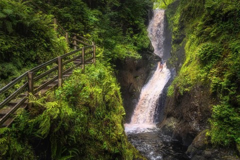 Spectacular wooden boardwalk on the hill with a view on tall waterfall and river in majestic