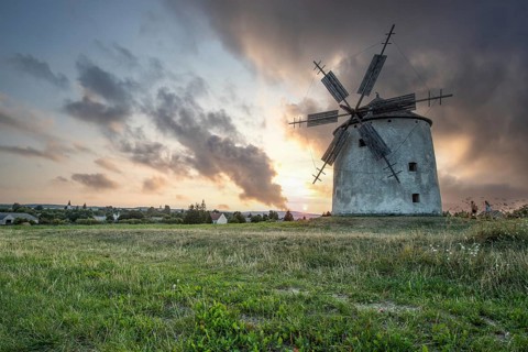 Windmill with wooden sails in a landscape with fields. Meadows and flowers appear in the sunset.