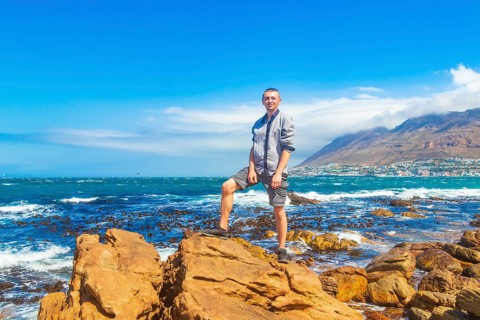 Male model tourist traveler at False Bay rough coast landscape with boulders waves and mountains