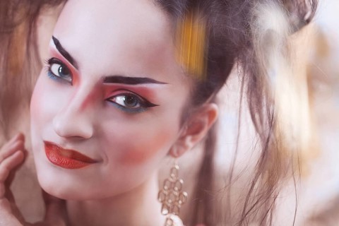 Close up stylized portrait of a Japanese geisha with bright make up standing at the window watching