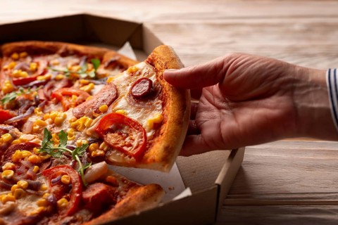 Human caucasian hand takes slice of large pizza from carton box on white wooden table