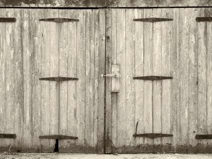 Monochrome old rural grey plank wooden plank doors with a bolt fastening and rusty iron hinges