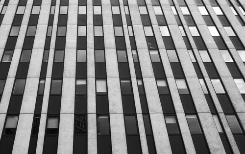 Close up perspective detail of tall high rise brutalist style office building with white vertical