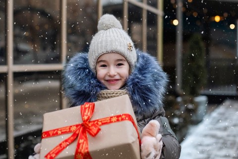 Portrait of joyful girl with a gift box for Christmas on a city street in winter with snow on a