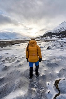 A woman in winter clothing on the frozen shore of the Ullsfjord, Sjursnes, Tromso, Troms, Norway,