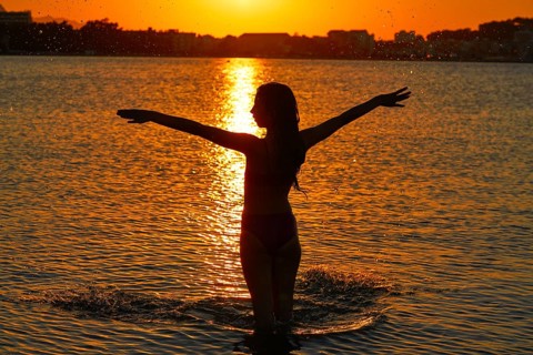 Girl silhouette at beach sunset open arms standing