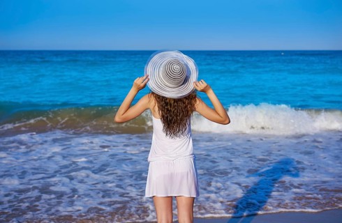 Girl with beach hat in sea open arms with summer white dress