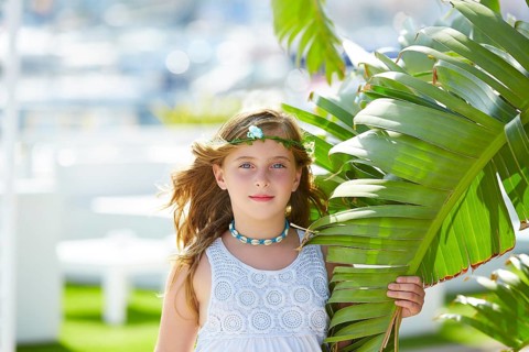 Blond kid girl at banana tree leaves in bright day light in Mediterranean