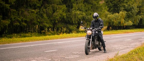 A motorcyclist wearing a helmet on a road adjacent to a forest
