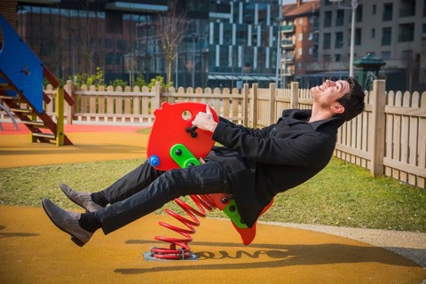Young man reliving his childhood plying in a childrens playground riding on a colourful red spring