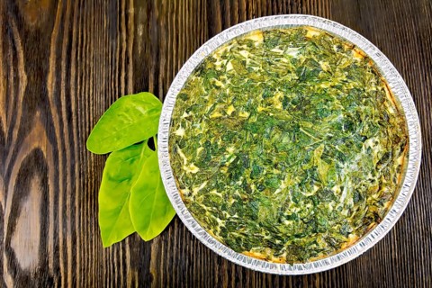 Celtic cake with spinach, tomatoes, oatmeal and eggs in baking dish from a foil, spinach leaves on