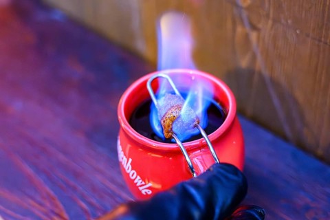 Red cup with burning sugar over mulled wine on a wooden bench, Straubing, Lower Bavaria