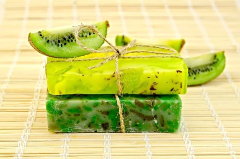 Two green homemade soap tied with twine, kiwi slices on a bamboo mat