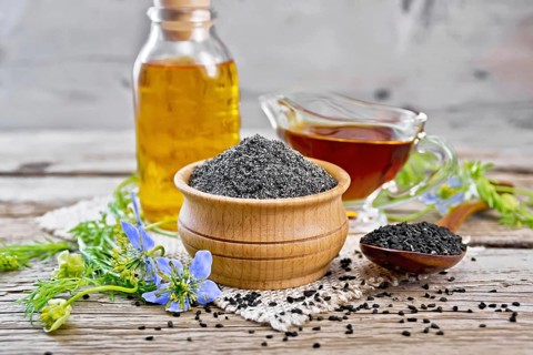 Flour of black caraway in a bowl, seeds in a spoon, oil in a bottle and sauceboat on burlap, sprigs