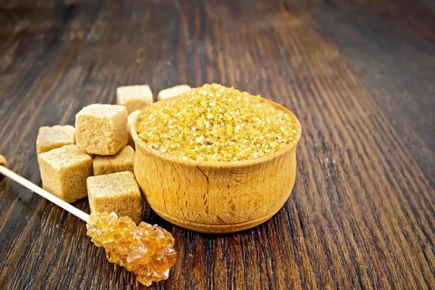 Granulated brown sugar in a bowl, crystalline on a stick and diced on a dark wooden board