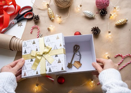 Key to house with keychain on cozy home in gift box with Christmas decor packaging. Pack present