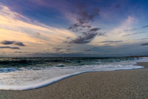 A low angle view of white sand beach with waves rolling in under a colorful sunset sky