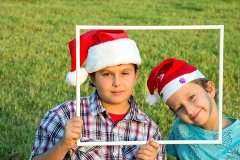 Two brothers in joke caps Santa Claus have fun smiling at the audience, holding a white frame.