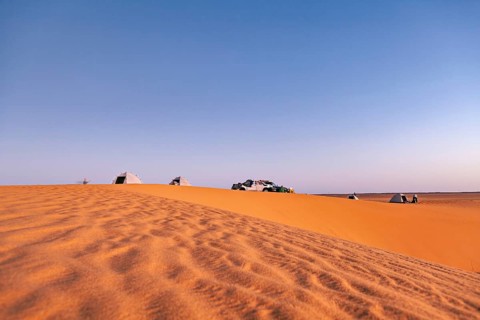 Tents and cars standing on a sand dune in the desert under a wide sky at sunset, camping in the