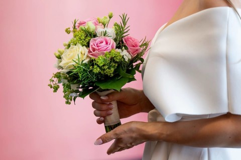 Bride holding bridal bouquet with roses in front of pink wall