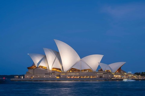 Illuminated Sydney Opera House at night train blue hour, surrounded by water, with unique
