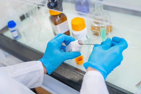Person in a laboratory puts a small amount of powder into a beaker with a spatula, Youth Research